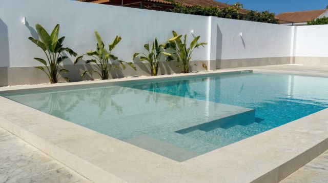 Piscina revestida con porcelánico blanco en jardín de vivienda unifamiliar